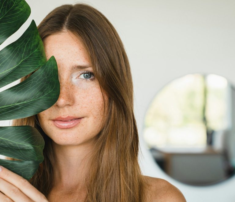 salon kosmetyczy krakow stymulatoryl woman covering her face with green leaf at home. Beauty and skin care concept